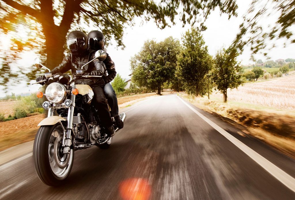 A motorcyclist rides their bike down the road with a passenger sitting behind them.