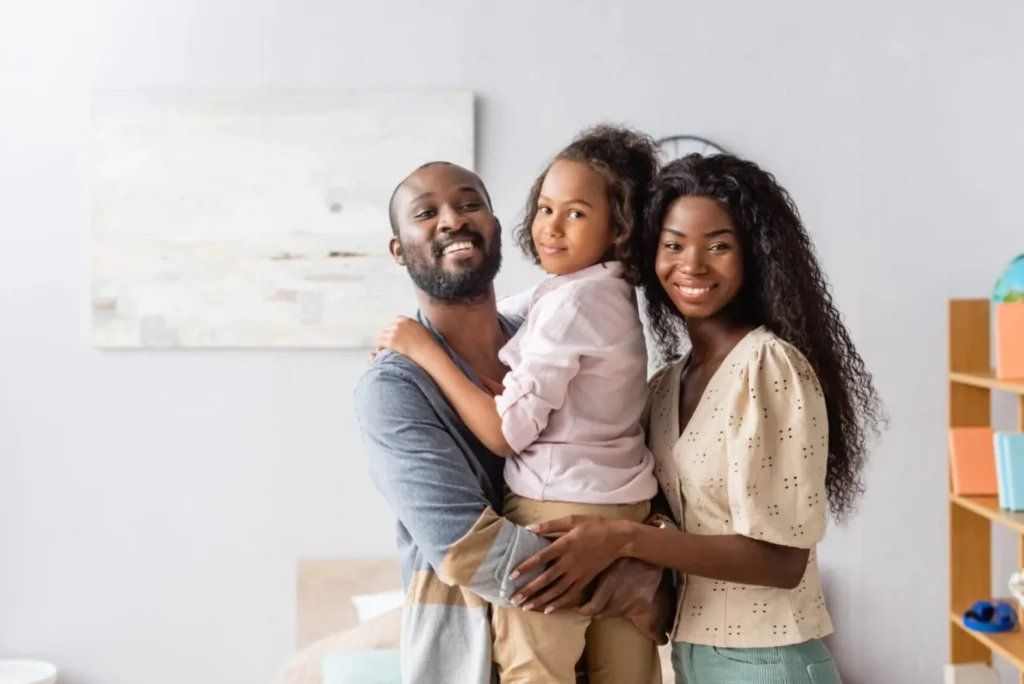 A happy couple smiles and holds their daughter in their home. They're happy because they sought out protection with the purchase of life insurance.