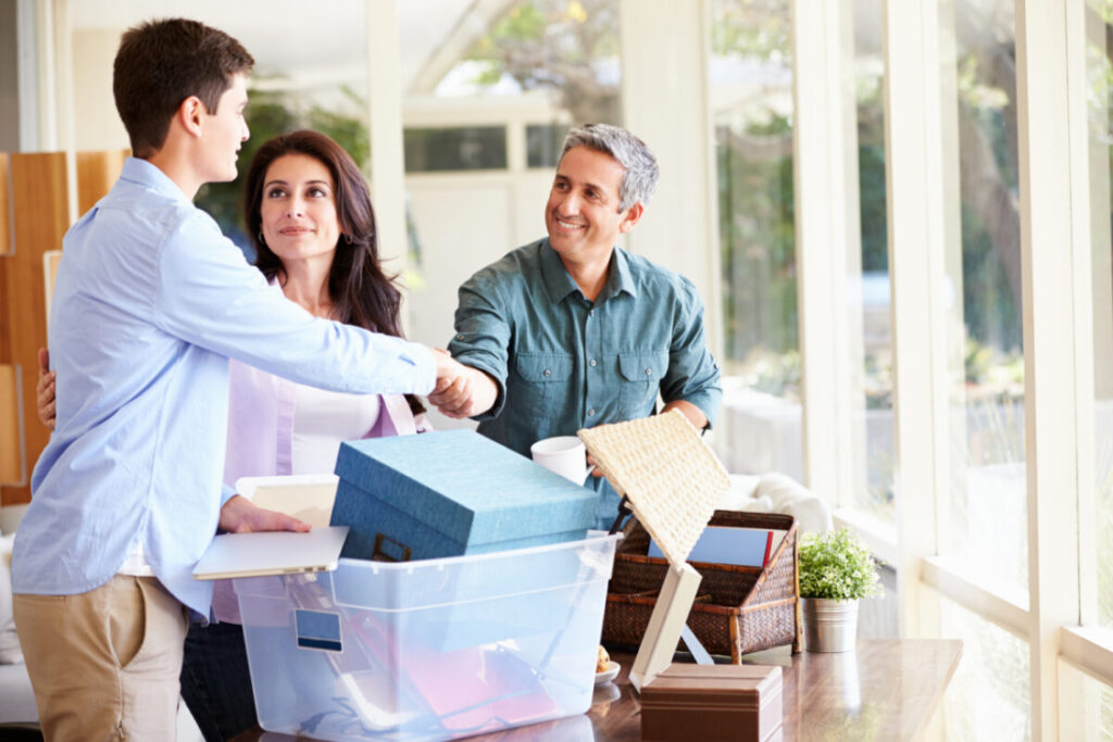 A teenager shakes hands with his father as his mother looks on as they continue packing.