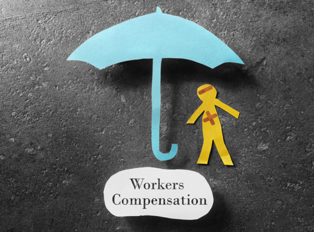 A picture featuring a paper cutout of a person standing underneath an umbrella with "Workers Compensation" written beneath it.