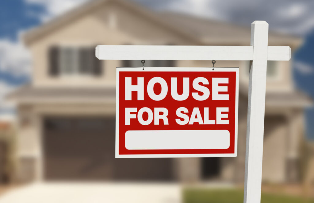 A real estate sign that says "House For Sale" in front of a two story house with a garage.