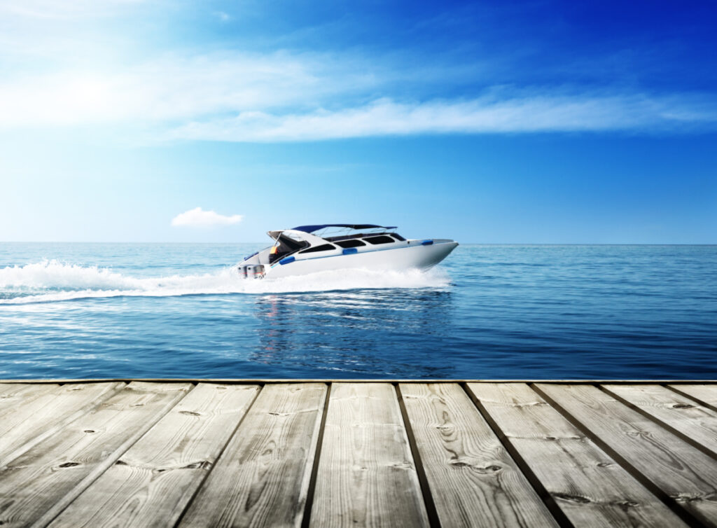 A boat drives around on the ocean. It is going fast. The perspective is from the dock as it is in the foreground.