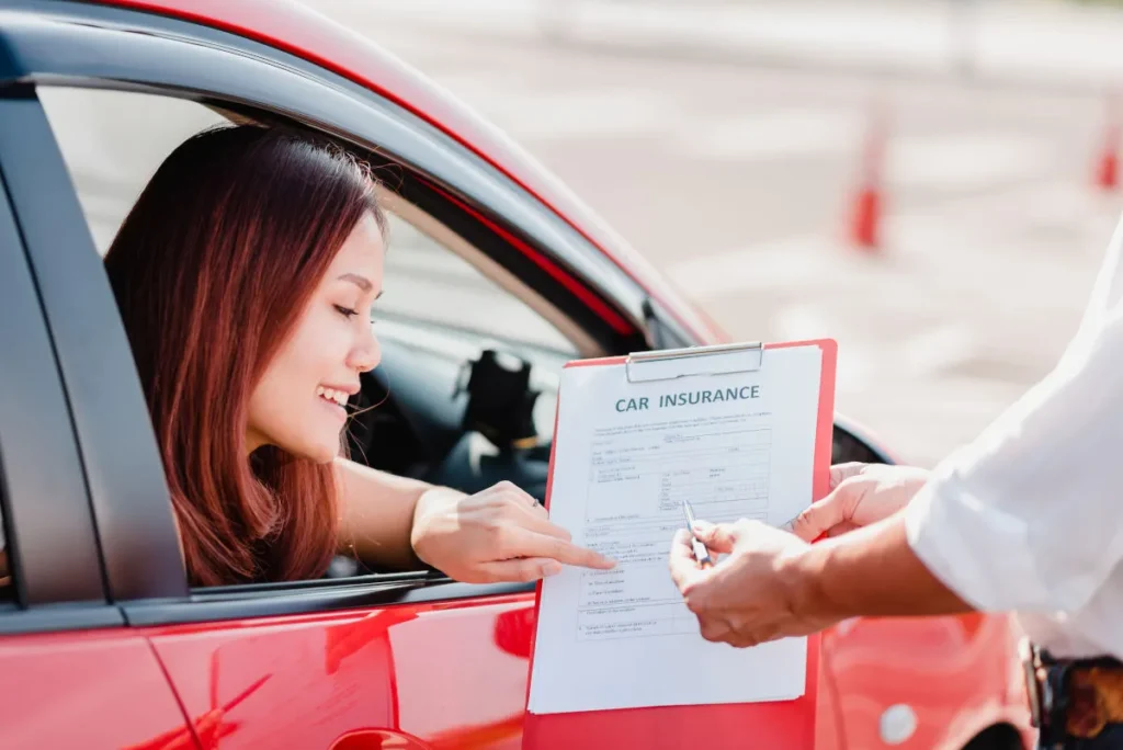 A woman sits in her car and looks over car insurance forms.
